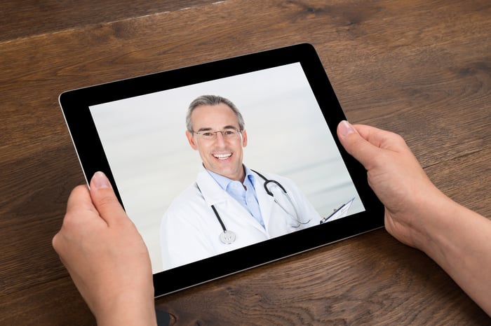 Two hands holding a tablet on which is the image of a doctor