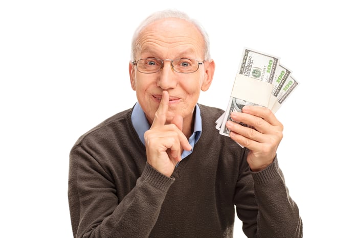 A senior citizen holding money and shushing as if to keep a secret. 