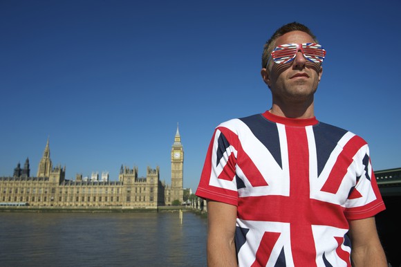 A man wearing a British flag shirt and glasses stands in front of Parliament.