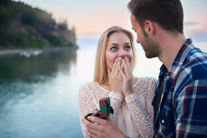 Young man proposing to surprised-looking girlfriend with ring in his hand