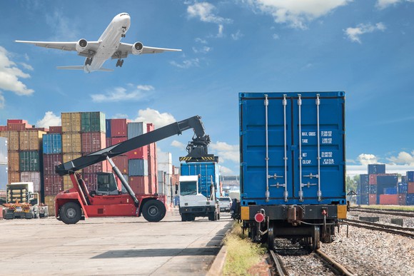 Freight being loaded onto trucks while an airplane flies overhead.