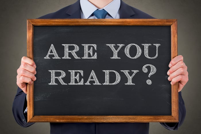 Someone in suit holding blackboard on which is written "Are you ready?"