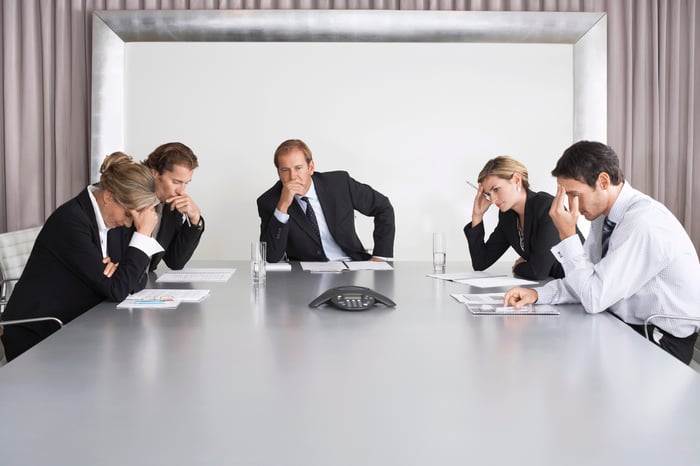 Business people sitting around a table, looking concerned.