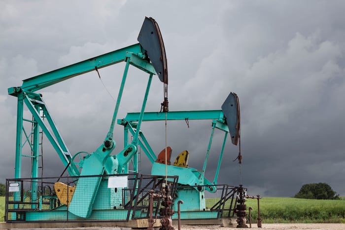 Two green oil wells sitting under a stormy grey sky.