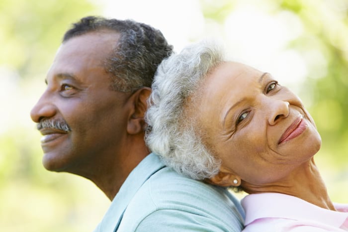 Senior couple sitting back to back and smiling