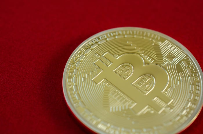 A physical bitcoin on a red background.