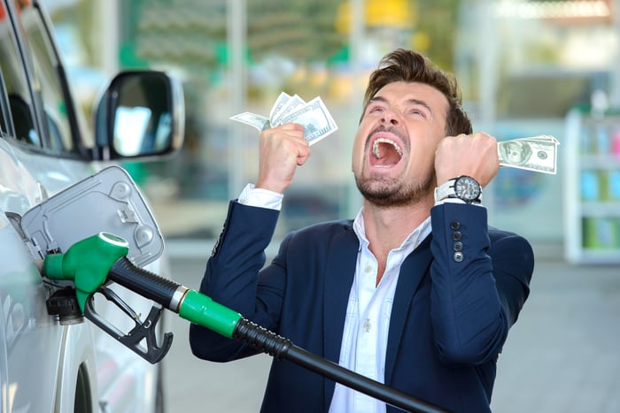 Emotional businessman counting money with gasoline refueling car at fuel station.