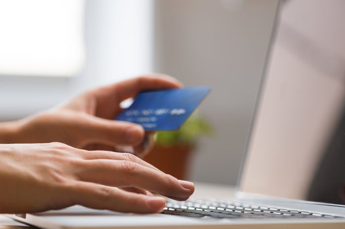 One hand holds a credit card while the other types on a keyboard. 