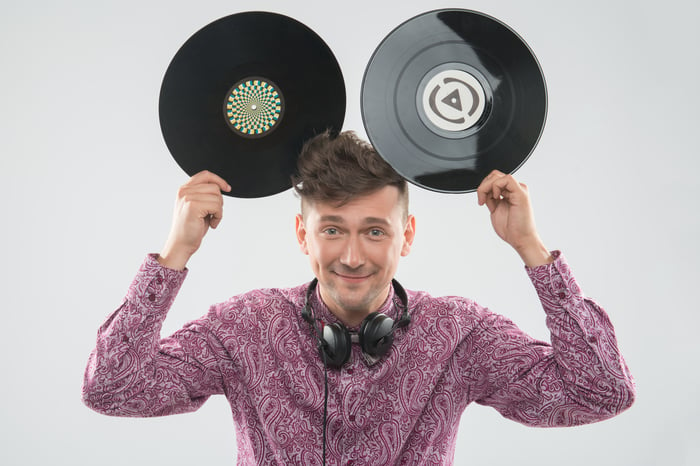 excited young DJ with stylish haircut, bow tie having fun with vinyl records - holding two up to his head like Mickey Mouse ears