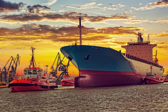 Big ship with escorting tugs leaving port at sunset.