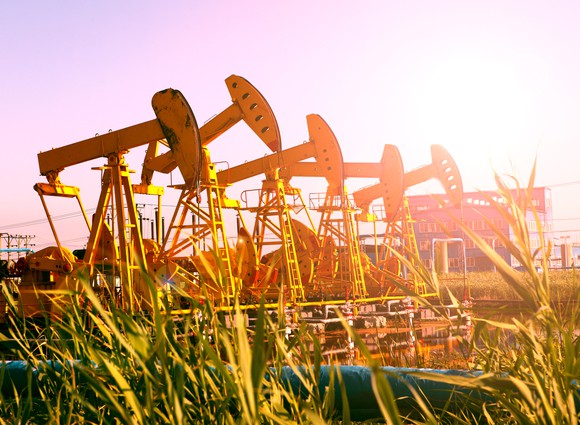 Several pumpjacks in a row with sunburst.