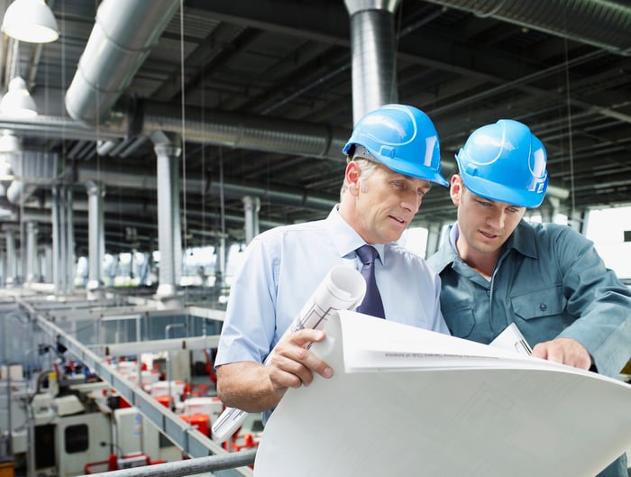 Two men looking at blueprints above a factory floor