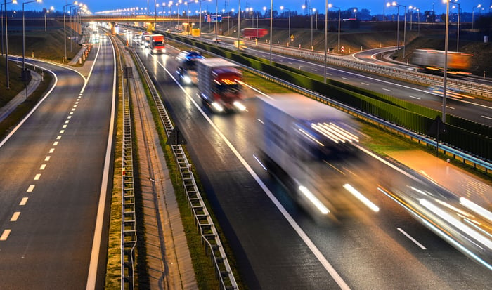 Long exposure shot of commercial trucks on highway at dusk.