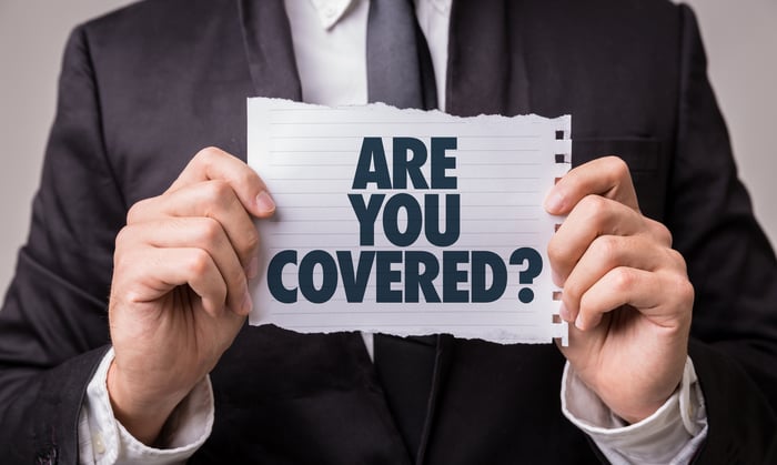 man in suit holding sign on which is printed the question "Are you covered?"