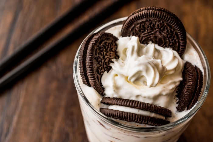 Milk shake on with whipped cream and cookies that look like Oreos on top.