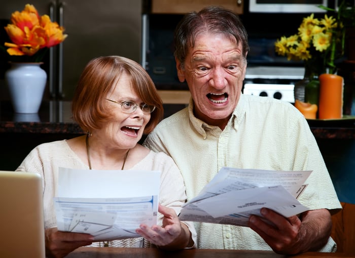 Older couple  holding medical bills and looking aghast, with mouths open