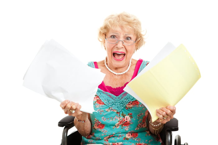 older woman with papers in each hand, looking apalled