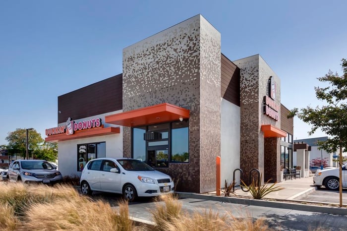 The exterior of a Dunkin' Donuts store, with cars lined up at the drive-through window.