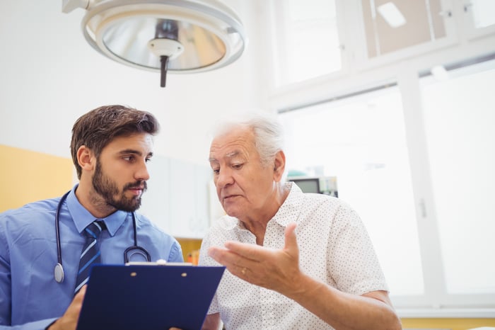 Senior man talking to doctor holding clipboard