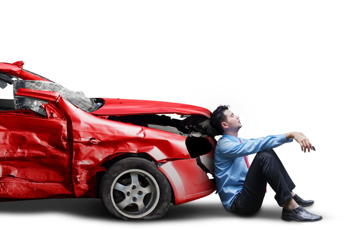 An upset man leaning on the front of a crashed car.