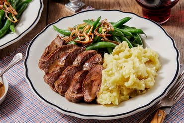 A plate of steak, mashed potatoes, and green beans