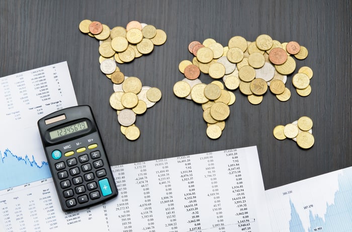 Coins laid out on a table in the shape of the continents and flanked by financial paperwork.