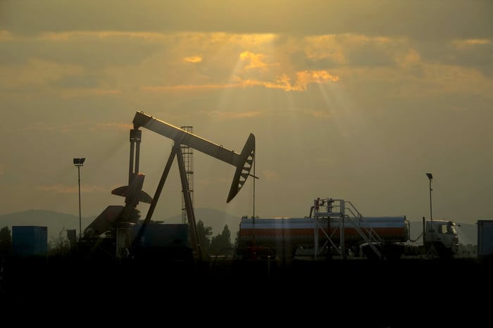 An oil pump with the sun breaking through behind the clouds in the background.