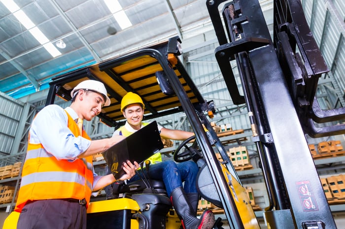 A man operating a forklift and talking with his supervisor. 