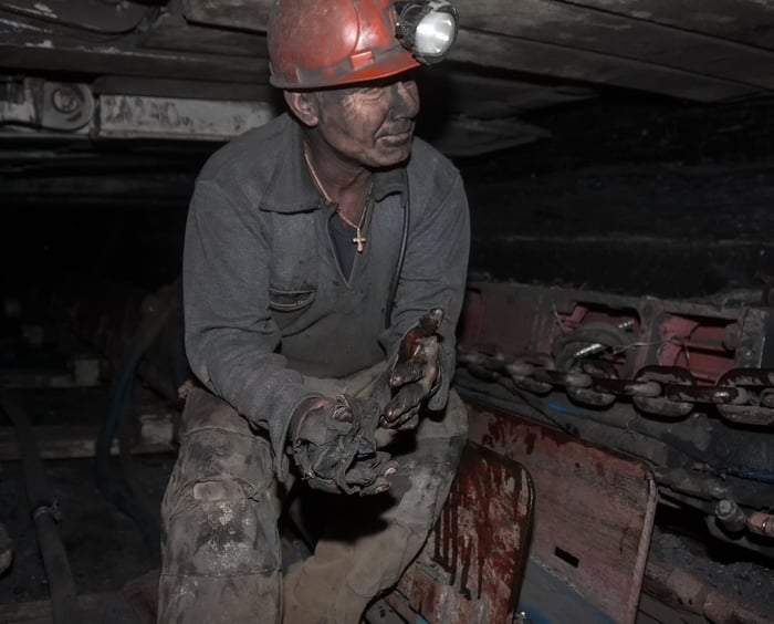 A coal miner standing, dirty, in a mine.