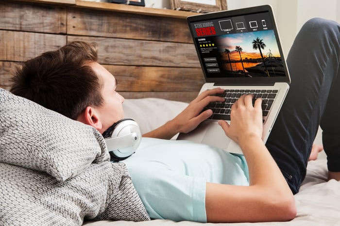 Man watching streaming series in a laptop computer, lying in the bed.