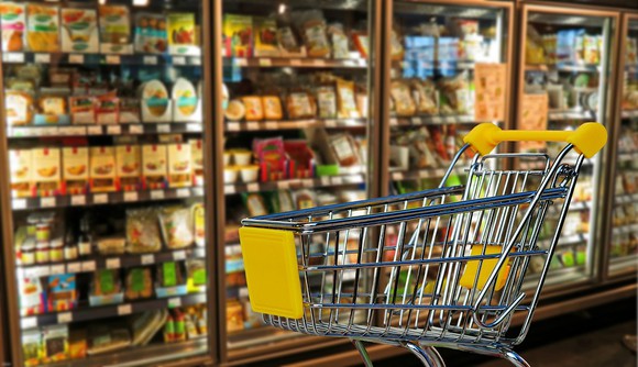 A grocery cart next to a supermarket freezer.