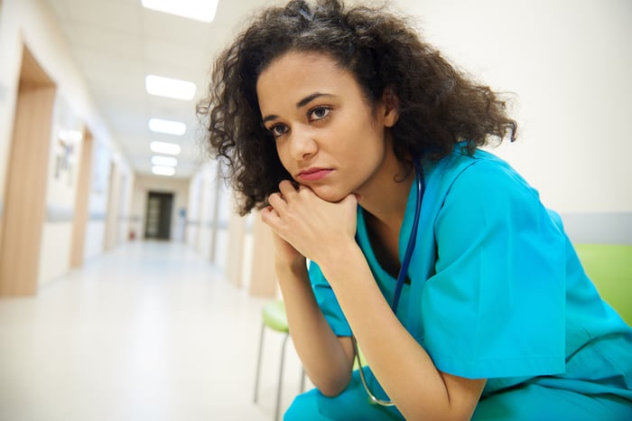 A worried nurse sitting in a hospital hallway.
