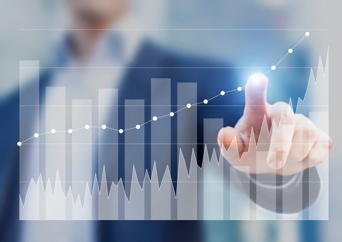 Businessman using finger to trace gains on transparent chart.