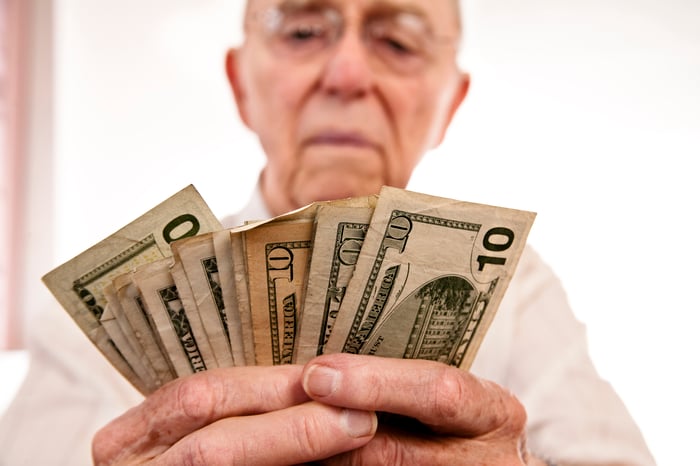 A senior citizen counting his Social Security income, with $10 bills fanned out in his hands.