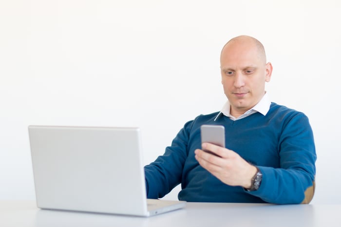 Man checking phone while working on laptop