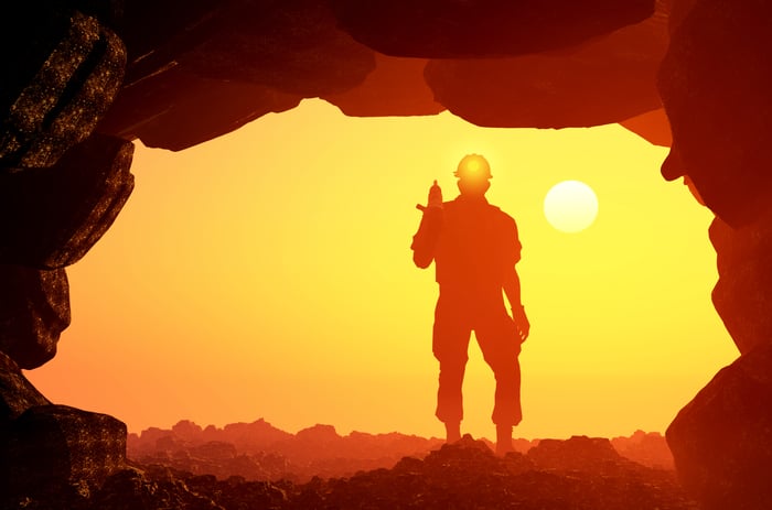 A man standing in the mouth of a mine with the setting sun in the distance.