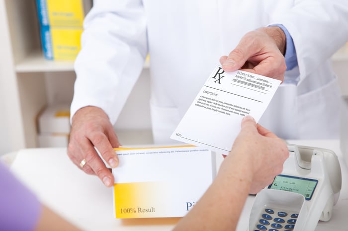 A pharmacist is handing a customer a perscription.