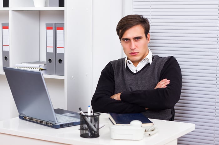 A displeased young worker with his arms folded at his desk. 