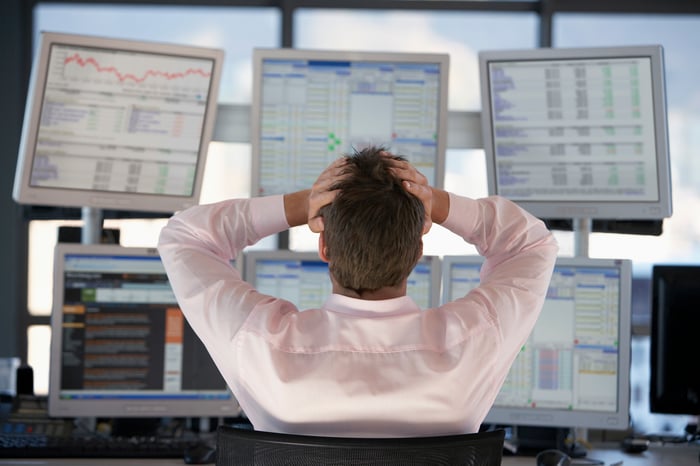 A frustrated stock trader grasping his head in front of computer screens. 