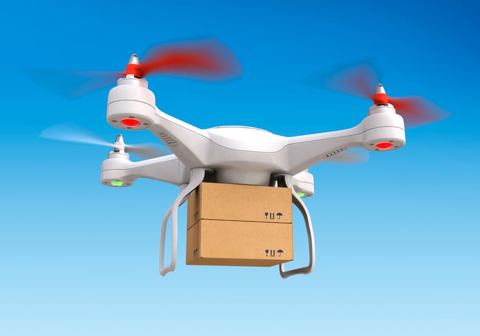 A delivery drone flying in sky carrying two cardboard boxes stacked one atop the other. Blue sky background.