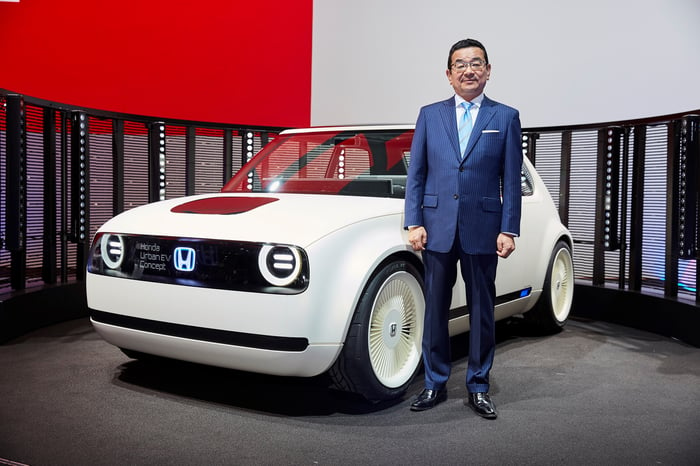 Hachigo, in a blue suit, stands next to the Urban EV Concept, a white hatchback with styling reminiscent of 1970s Honda Civics, on Honda's stand at the 2017 International Motor Show in Frankfurt, Germany.