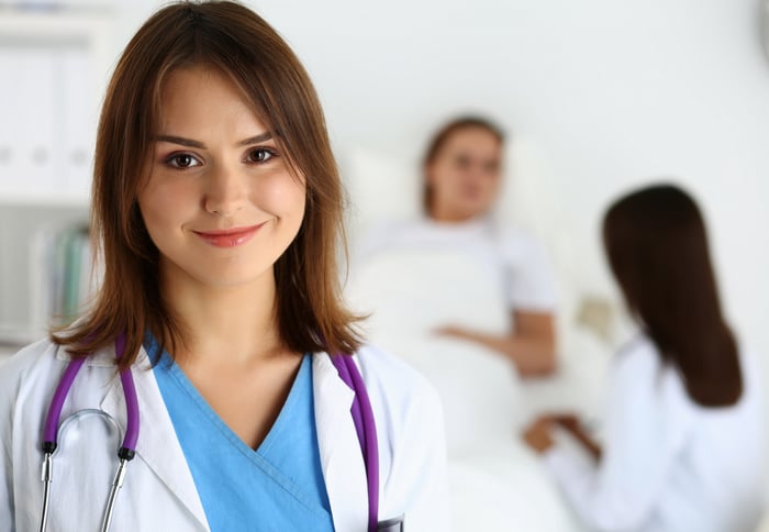 Smiling woman in scrubs and white coat