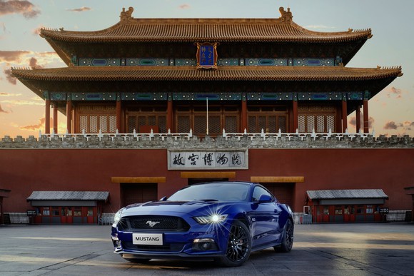A blue Ford Mustang in front of a traditional Chinese building.