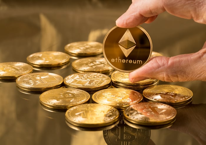 A person holding a physical gold Ethereum coin above a stack of Ethereum coins. 