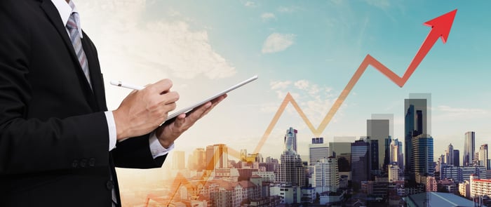 Businessman working on a tablet with a city panorama in the background and and rising arrow.