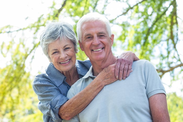 Smiling senior woman putting arms around smiling senior man.