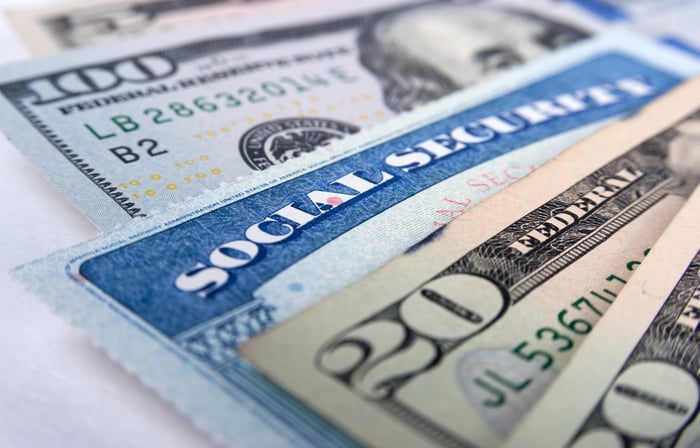 A Social Security card wedged in between a fanned pile of cash bills.