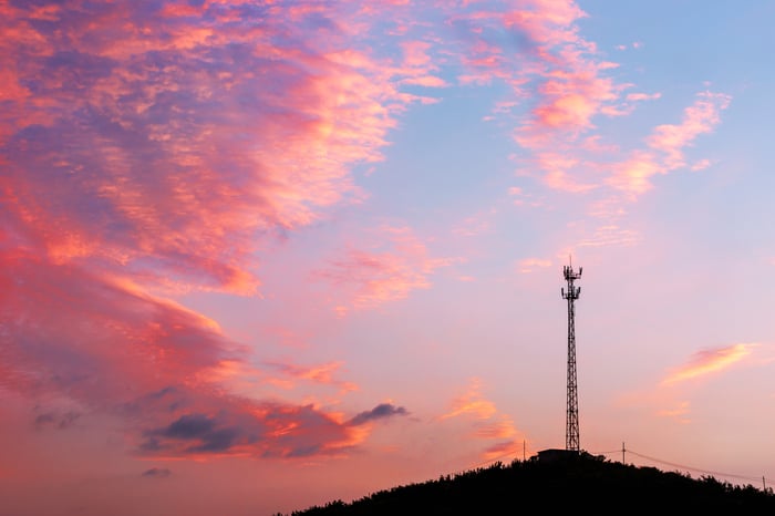 A communications tower on top of a hill with brightly colored clouds in the background.