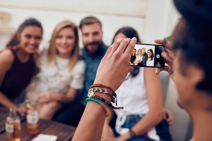 young man taking photo of four friends with smartphone