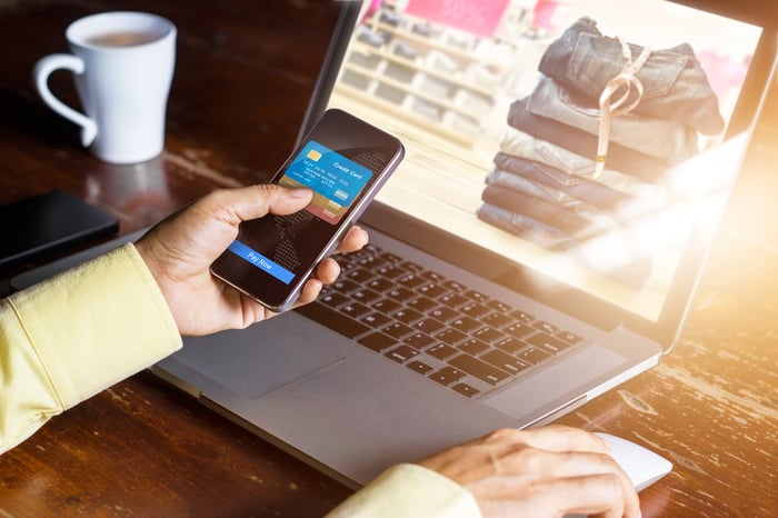 A person using a mobile wallet on their smartphone to buy pants on their laptop screen. 